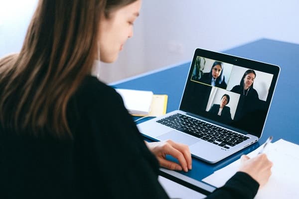 Professional woman attending a virtual meeting on her computer & taking notes